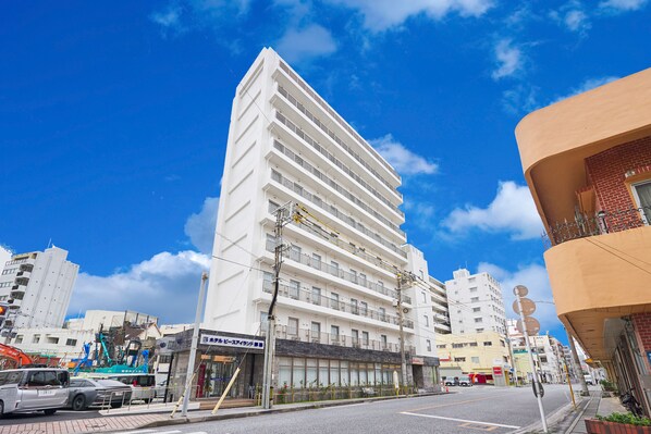 Un hotel moderno a più piani, con balconi su ogni piano, situato in una vivace via cittadina, con altri edifici e veicoli nelle vicinanze.
