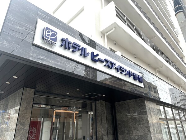 Fachada moderna de un hotel, con un letrero destacado y acceso por puerta de vidrio.