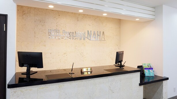 A hotel reception desk with a marble wall, two monitors, a nameplate, and a small display stand with brochures. - Hotel Peace Island Naha (Naha)