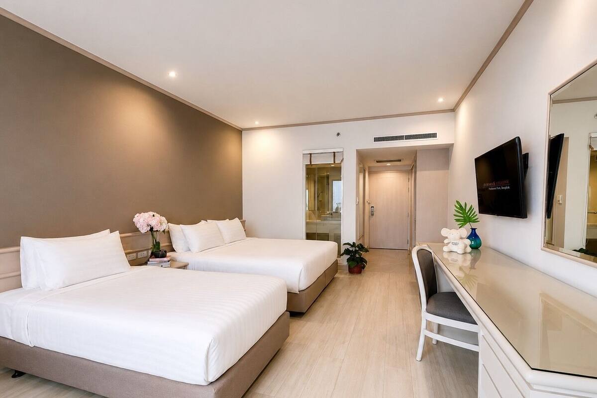 Una habitación de hotel con dos camas, un escritorio, una silla, un televisor y un espejo.