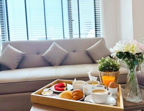 A breakfast tray with pastries, coffee, and juice on a wooden tray, a vase with flowers, and a sofa in the background. - FuramaXclusive Pratunam Park Hotel (Bangkok)