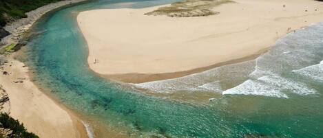 Eine Küstenlandschaft mit Sandstrand, klarem türkisblauem Wasser und einer kleinen Siedlung mit Gebäuden auf einem Hügel.