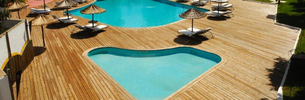 A wooden deck with a pool, lounge chairs, and umbrellas.
