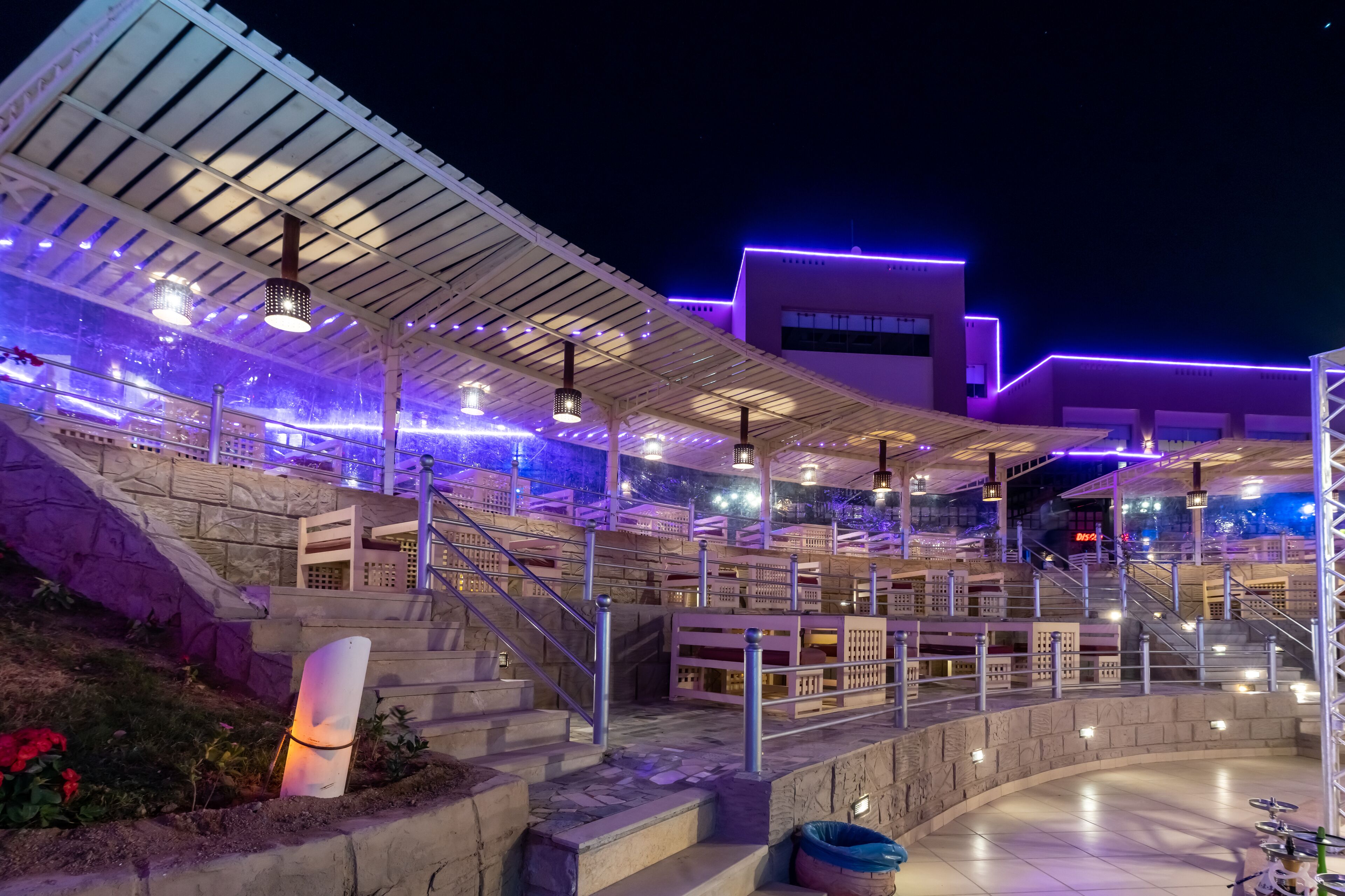 A modern outdoor area with a covered seating area, multiple levels of steps, and a building in the background.