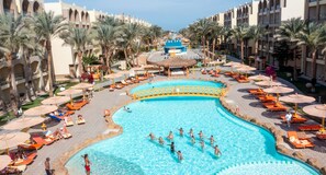 A large pool surrounded by sun loungers and umbrellas, with palm trees and a hotel building in the background. - El Karma Aqua Beach Resort (Hurghada)