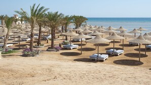 A beach with rows of sun umbrellas and lounge chairs, palm trees, and a clear view of the sea. - El Karma Aqua Beach Resort (Hurghada)