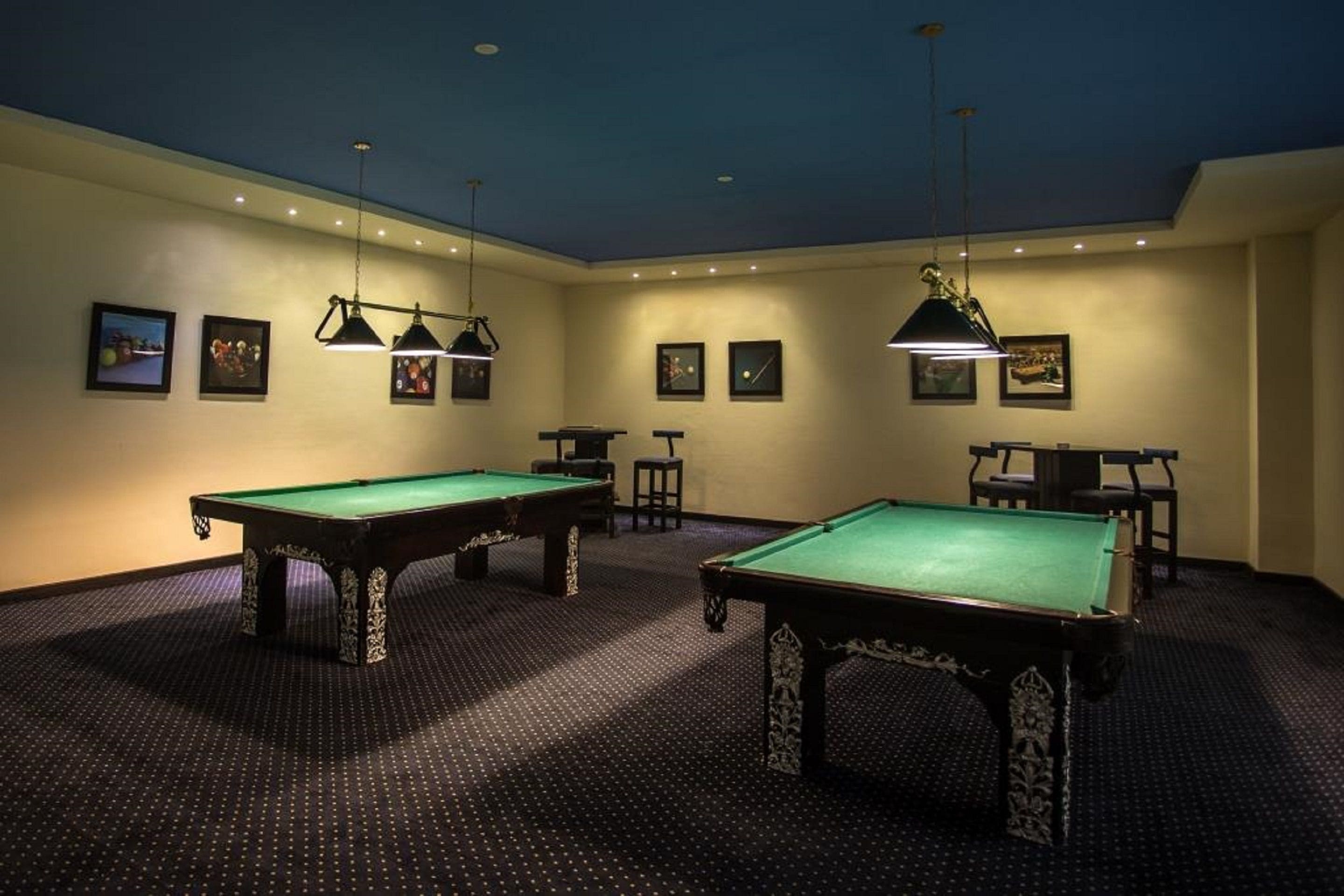 A room with two pool tables, a ceiling with recessed lighting, and framed pictures on the walls.