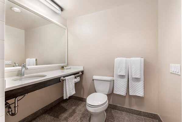 Un bagno moderno con lavandino, specchio e servizi igienici bianchi. Asciugamani appesi al muro e un portascopevoli.