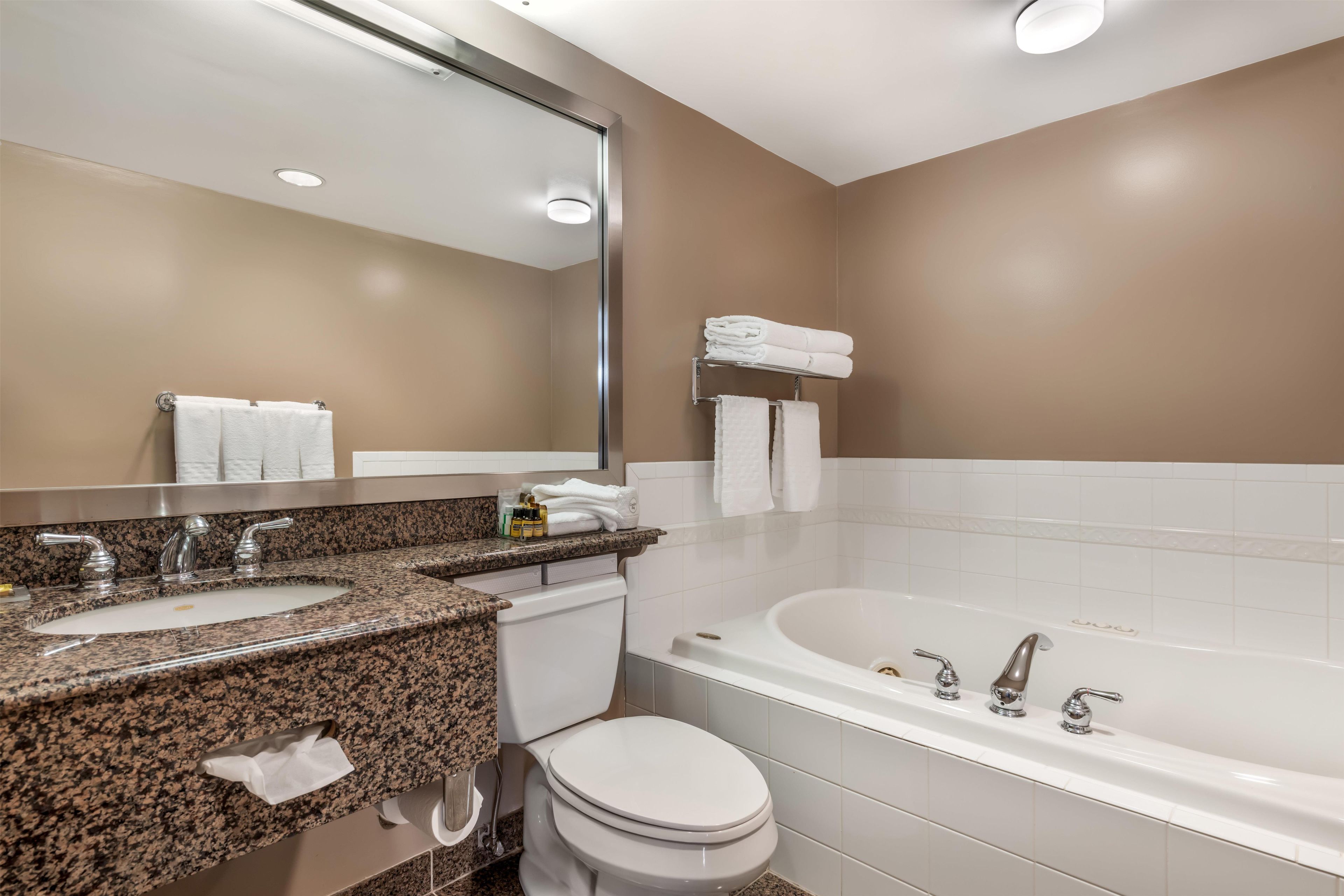A modern bathroom with a granite countertop sink, a toilet, and a bathtub.
