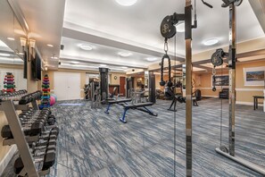 Un gimnasio con diverso equipamiento de ejercicio, incluyendo mancuernas, máquinas de pesas y una máquina de poleas.