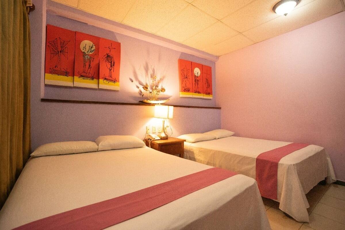 Una habitación de hotel con dos camas, una mesita de noche con lámpara y decoración en la pared.