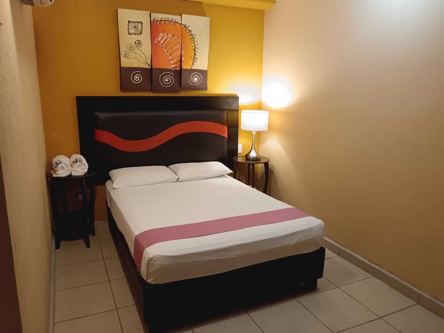 Une chambre d’hôtel avec un lit, une table de chevet avec des serviettes, une lampe et une œuvre d’art accrochée au mur au-dessus du lit.