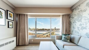 A modern living room with a large window, a sofa, a table, and framed pictures on the wall. - Park Town Hotel (Saskatoon)