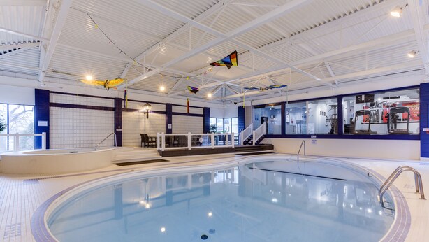 An indoor swimming pool with a tiled floor, a staircase leading to a viewing area, and a clear ceiling with hanging decorations. - Park Town Hotel (Saskatoon)