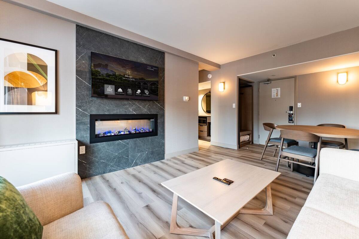 A modern living room with a fireplace, a flat-screen TV mounted on a marble wall, and a dining area with a wooden table and chairs.