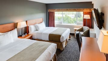 Ein Hotelzimmer mit zwei Betten, einem Schreibtisch, einem Sessel, einem Fernseher und einem Fenster mit Vorhängen.