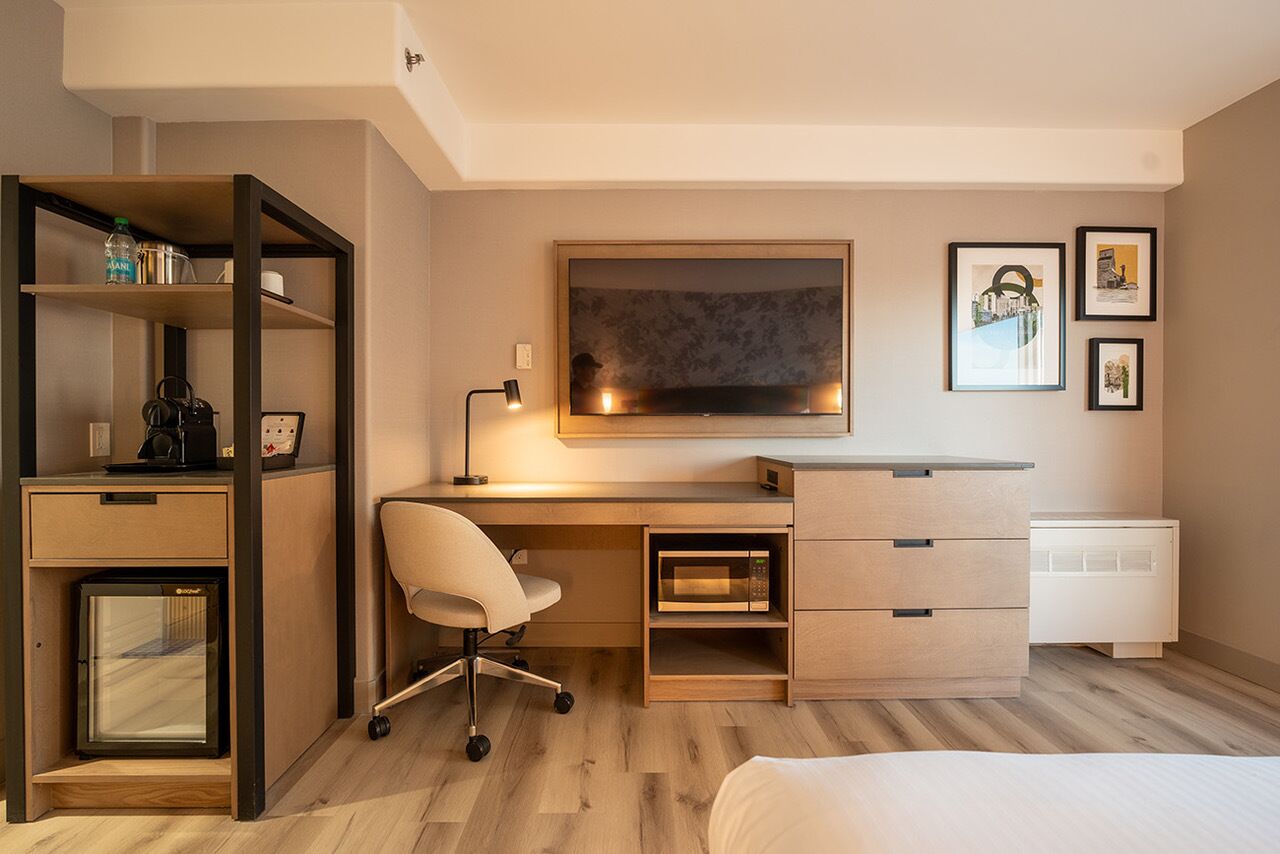 Un dormitorio moderno con cama, escritorio con silla, estantería, microondas y radiador.