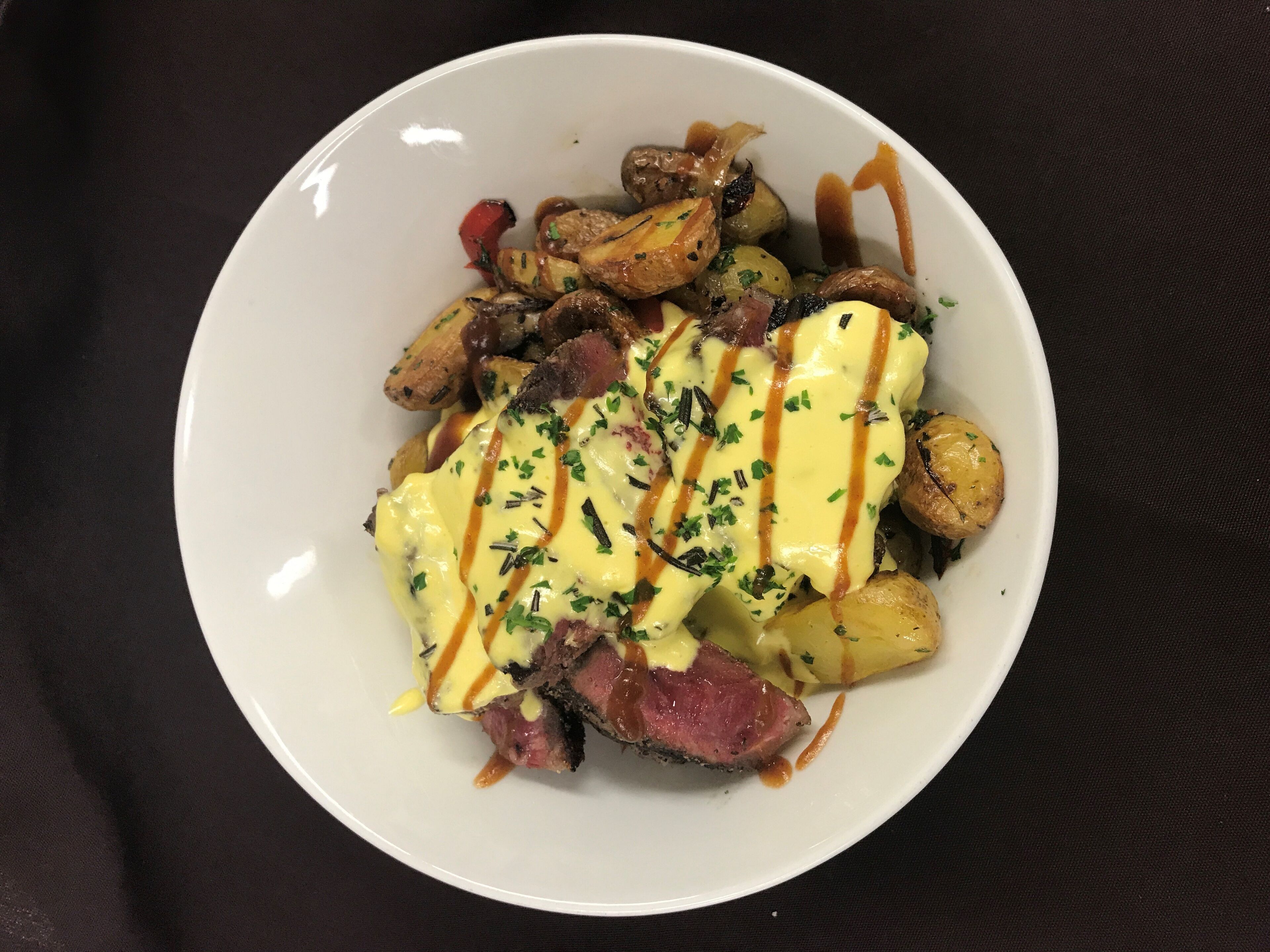 A white plate with a steak topped with sauce, surrounded by roasted potatoes and mushrooms.
