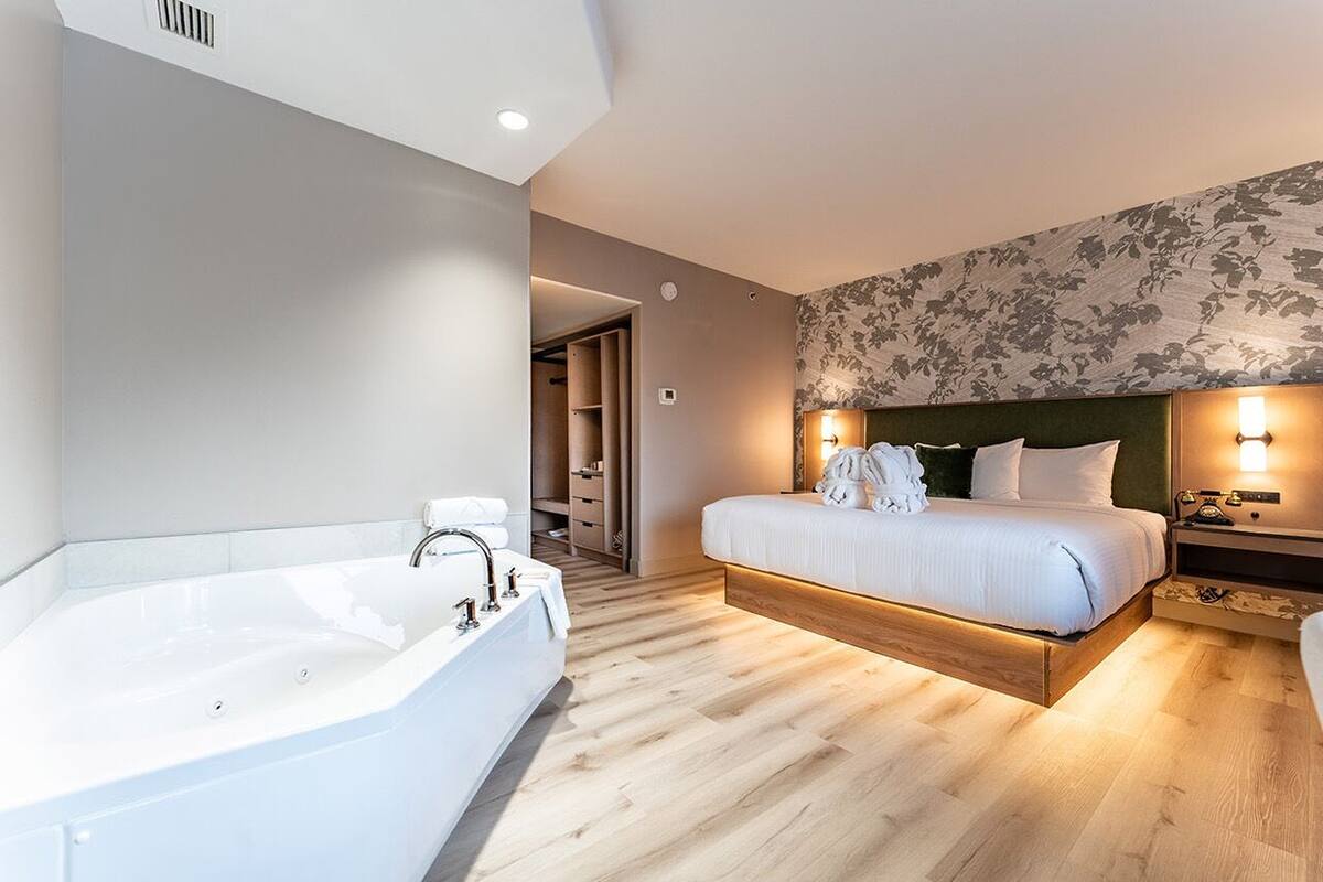 A modern bedroom with a large bed, a separate bathtub, and a walk-in closet.