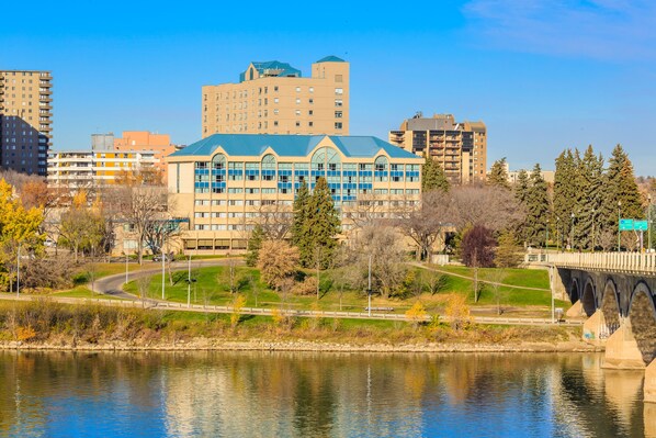 A large building with a blue roof and multiple windows, surrounded by trees and a body of water. - Park Town Hotel (Saskatoon)