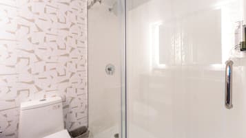 Um banheiro com vaso sanitário, chuveiro com porta de vidro e parede com padrão geométrico.