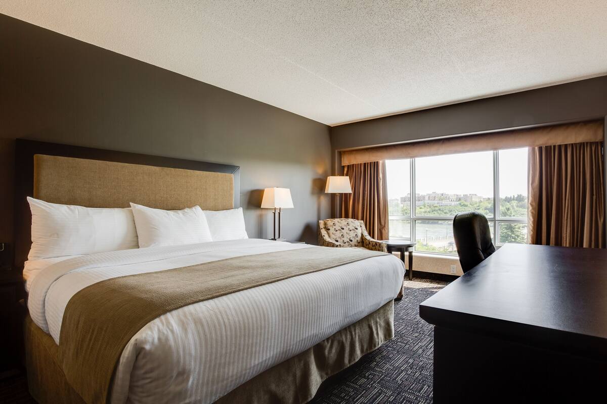 A hotel room with a large bed, a desk, two chairs, and a window with a view.