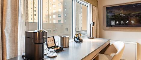 Una habitación de hotel moderna con un ventanal grande, una estación de café y una pantalla digital que muestra información de la habitación.