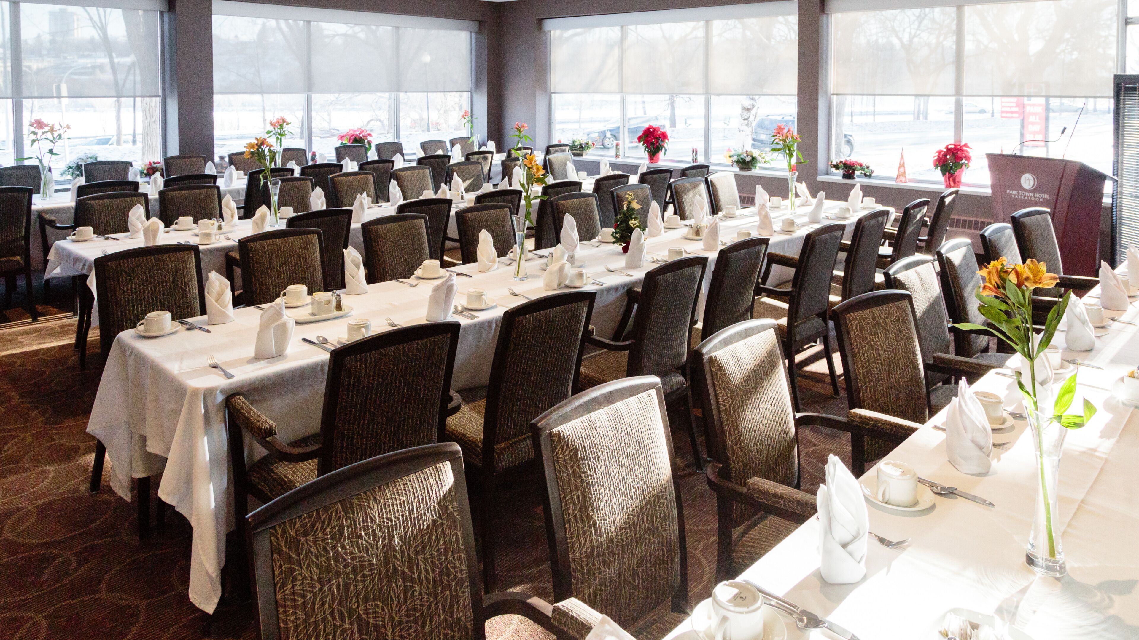A large conference room with rows of tables set for a formal event, equipped with chairs, tables, and floral centerpieces.