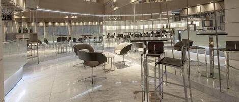 A spacious, modern interior with high ceilings, a central open area with seating, and a kitchen area visible through a glass partition.