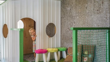 A children's playhouse with a green roof, white walls, and a wooden door.