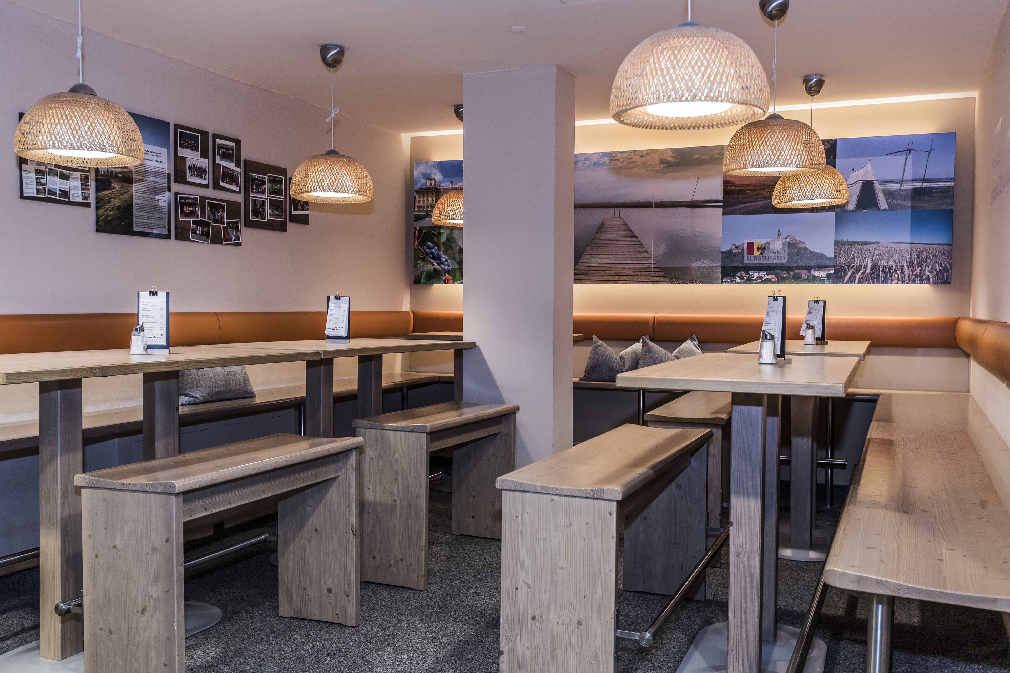 Un restaurante moderno con mesas y bancos de madera, lámparas colgantes tejidas y una pared decorada con diversas fotografías.