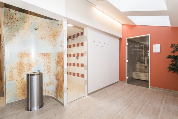 Un intérieur moderne avec une porte en verre donnant sur un espace douche, une poubelle et un mur orné d’un motif texturé original.