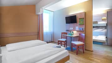Une chambre d’hôtel avec un grand lit, un bureau avec des chaises, une télévision et une petite kitchenette.