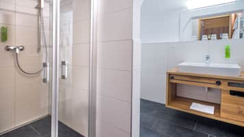 Et moderne badeværelse med en glasafskærmet brusekabine, et træbord med vask og et spejl over bordet.