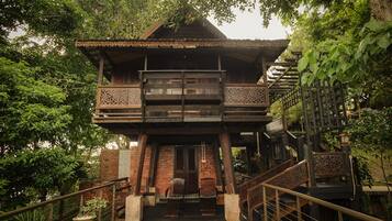 A traditional wooden house with a balcony, surrounded by lush greenery.