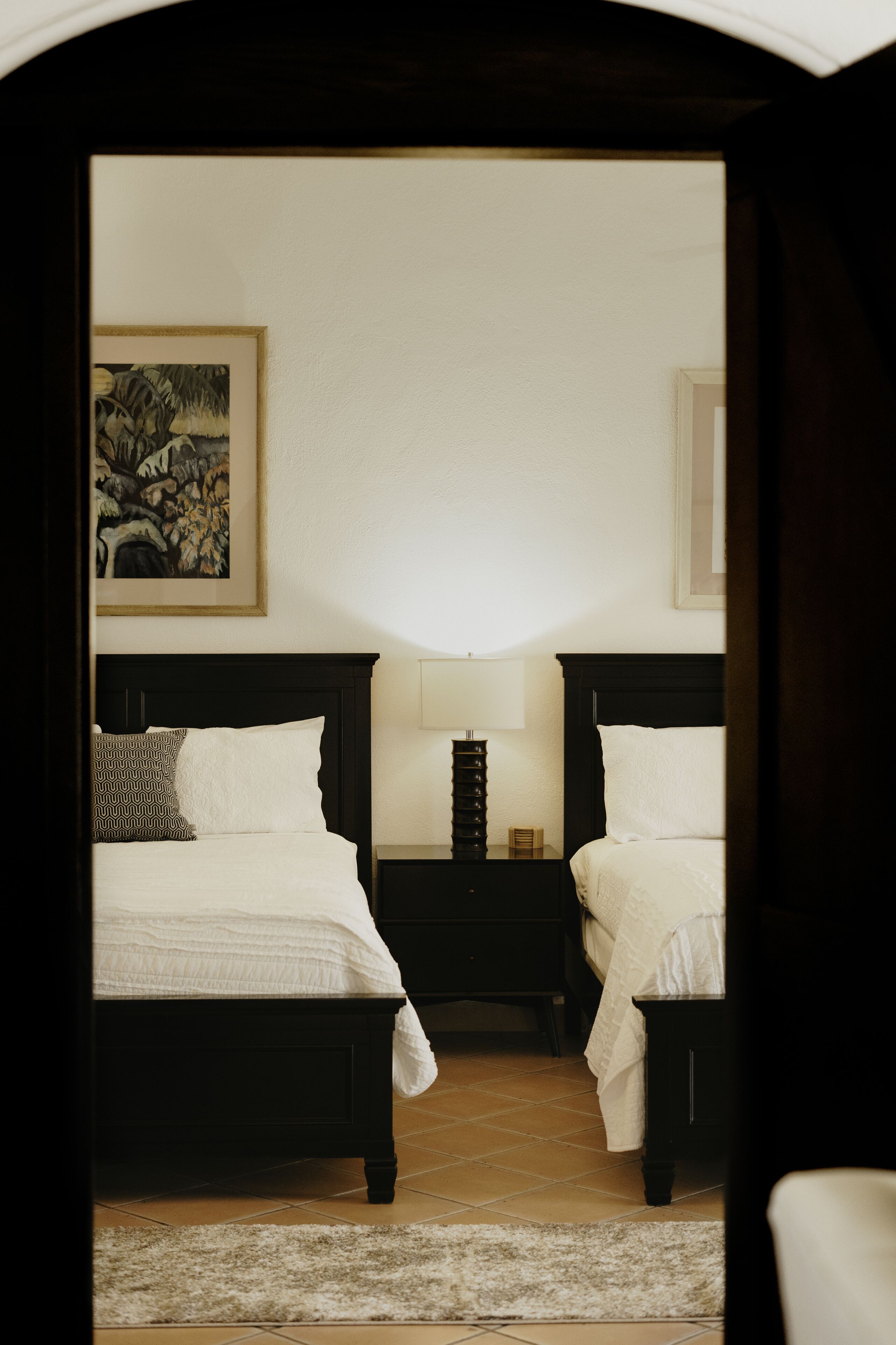Ein Hotelzimmer mit zwei Betten, einem Nachttisch, einer Lampe und einem gerahmten Bild an der Wand.