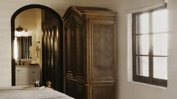 A bedroom with a large bed, a wardrobe, a window, and a bathroom visible through an archway.