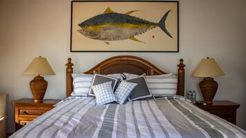 A neatly made bed with striped bedding, two bedside tables with lamps, and a framed fish painting on the wall.
