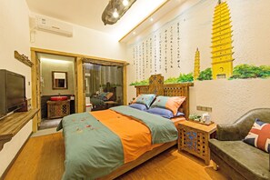 A bedroom with a bed, a wooden nightstand, a TV, a red sink, and a wall with a mural of a pagoda. - China Old Story Inns Dali Ancient Town (Dali)