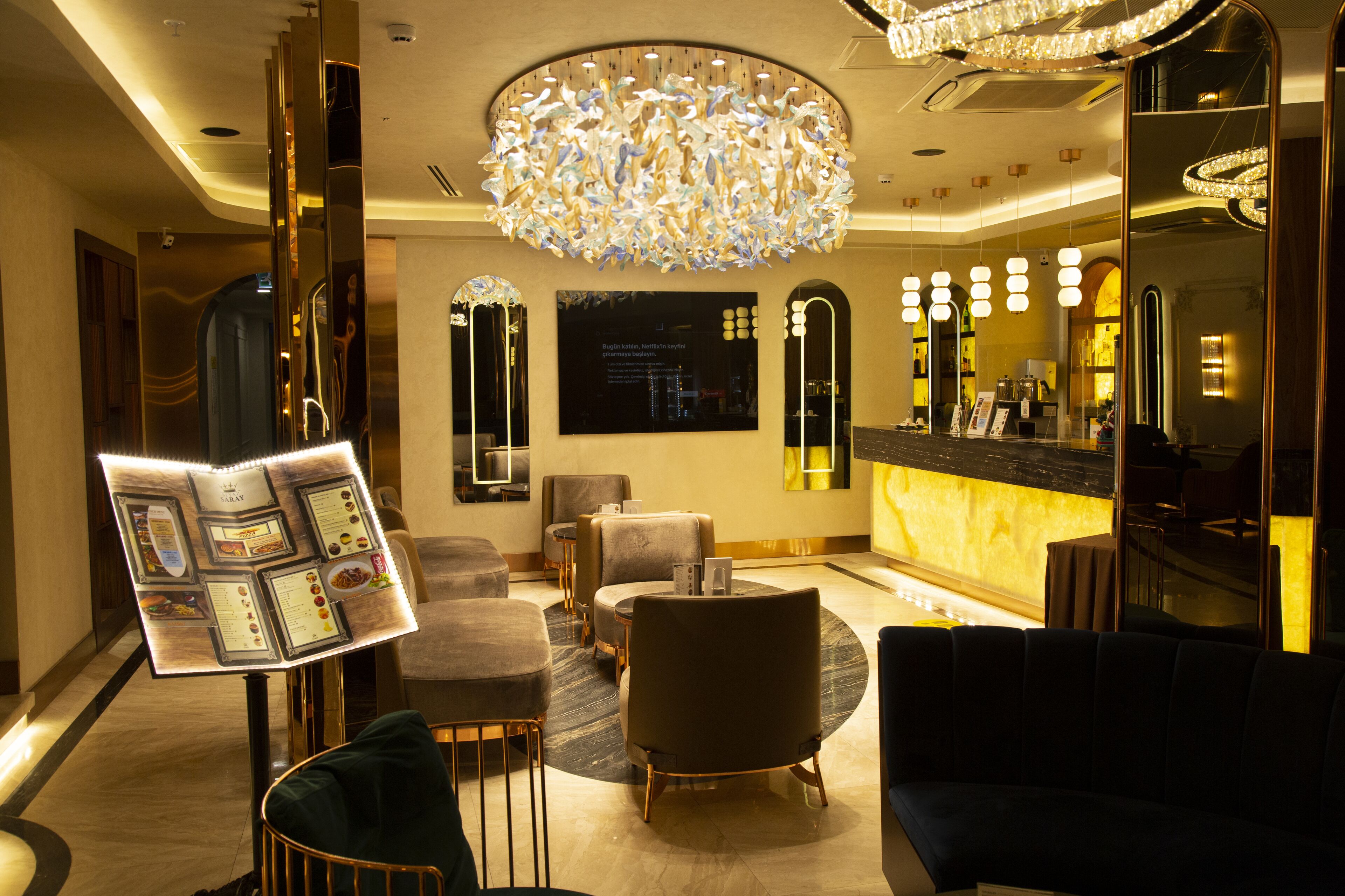A modern lobby with a central chandelier, seating areas, and a reception desk.