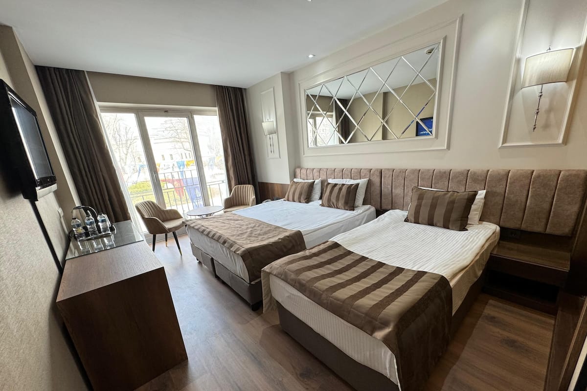 Habitación de hotel con dos camas, un escritorio, una silla, un televisor y una ventana con cortinas.