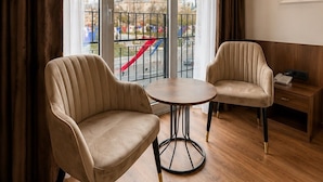 Habitación de hotel con dos sillones, una mesita redonda, una mesita de noche con lámpara y vistas a un edificio con cúpula a través de amplias ventanas.