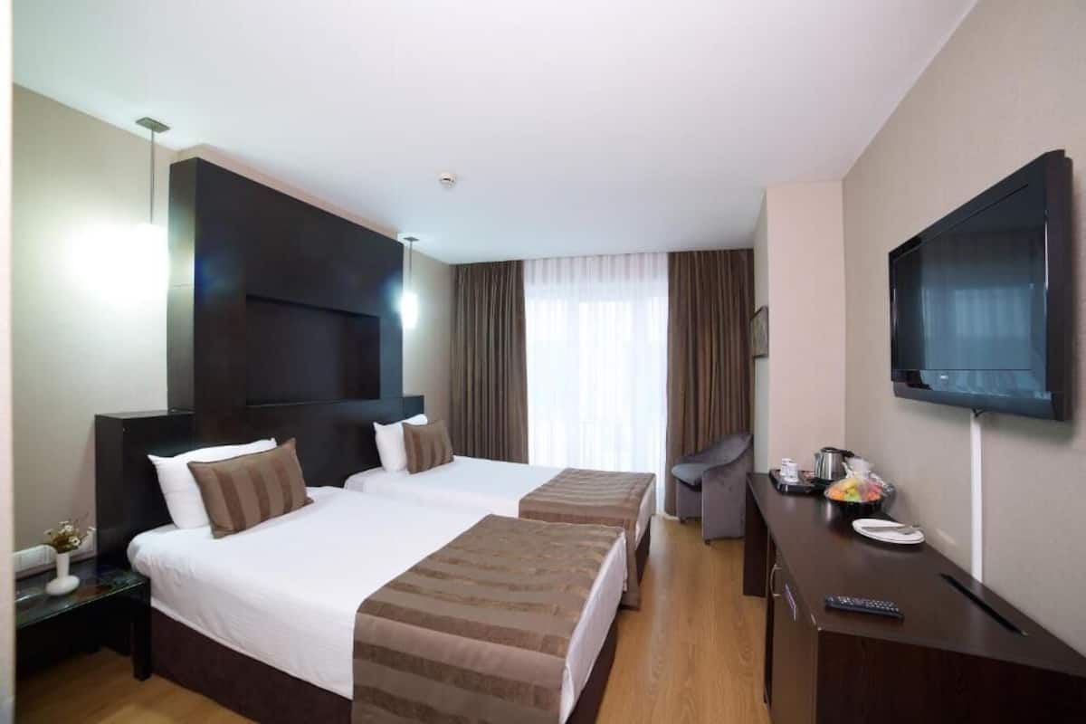Una habitación de hotel con dos camas, televisión, escritorio con control remoto y ventana con cortinas.