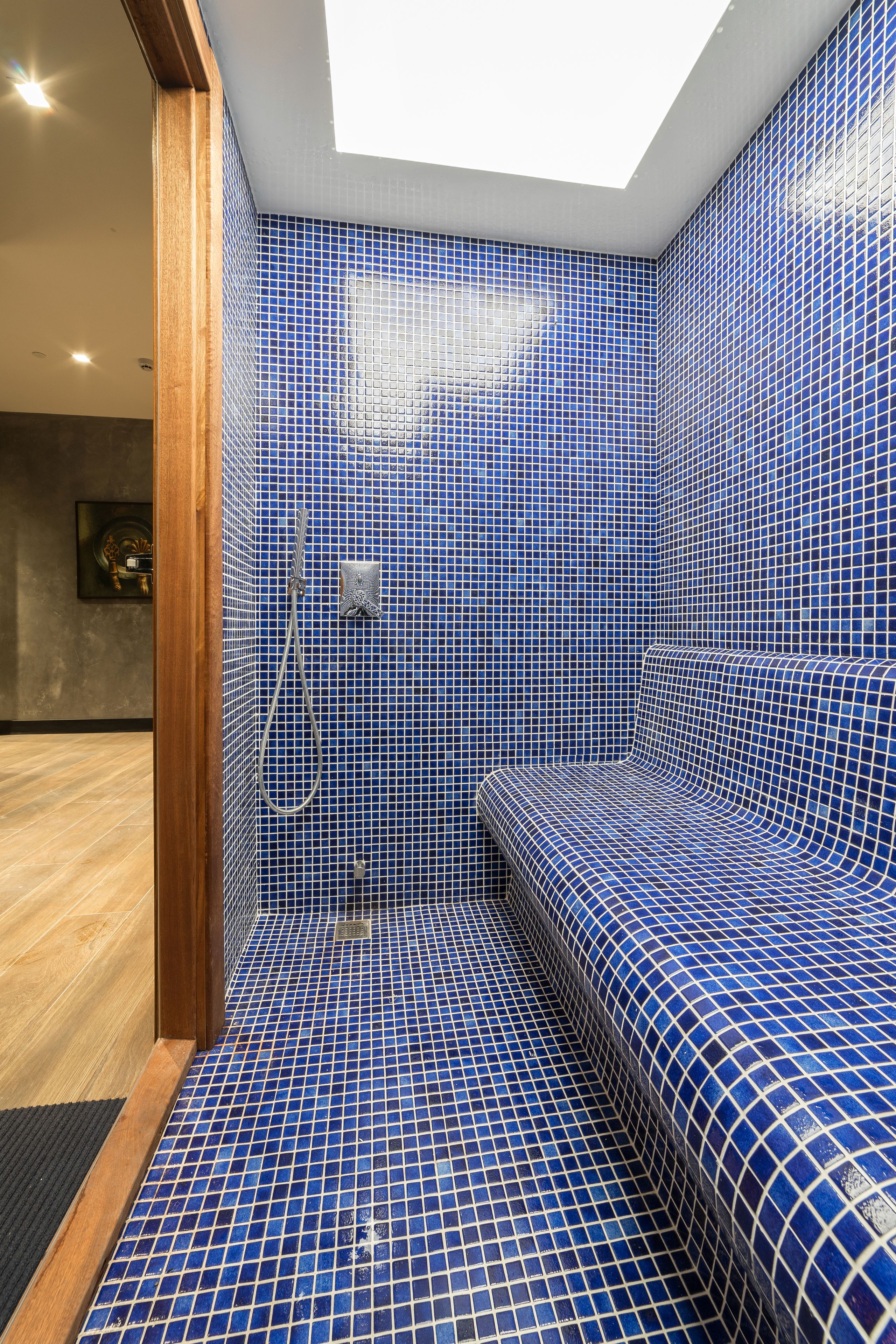 Un bagno con piastrelle blu a mosaico, una doccia e una panchina.