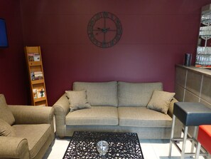 A living room with a sofa, a coffee table, a bookshelf, and a clock on the wall. - Hôtel Saint Daniel (Peruwelz)