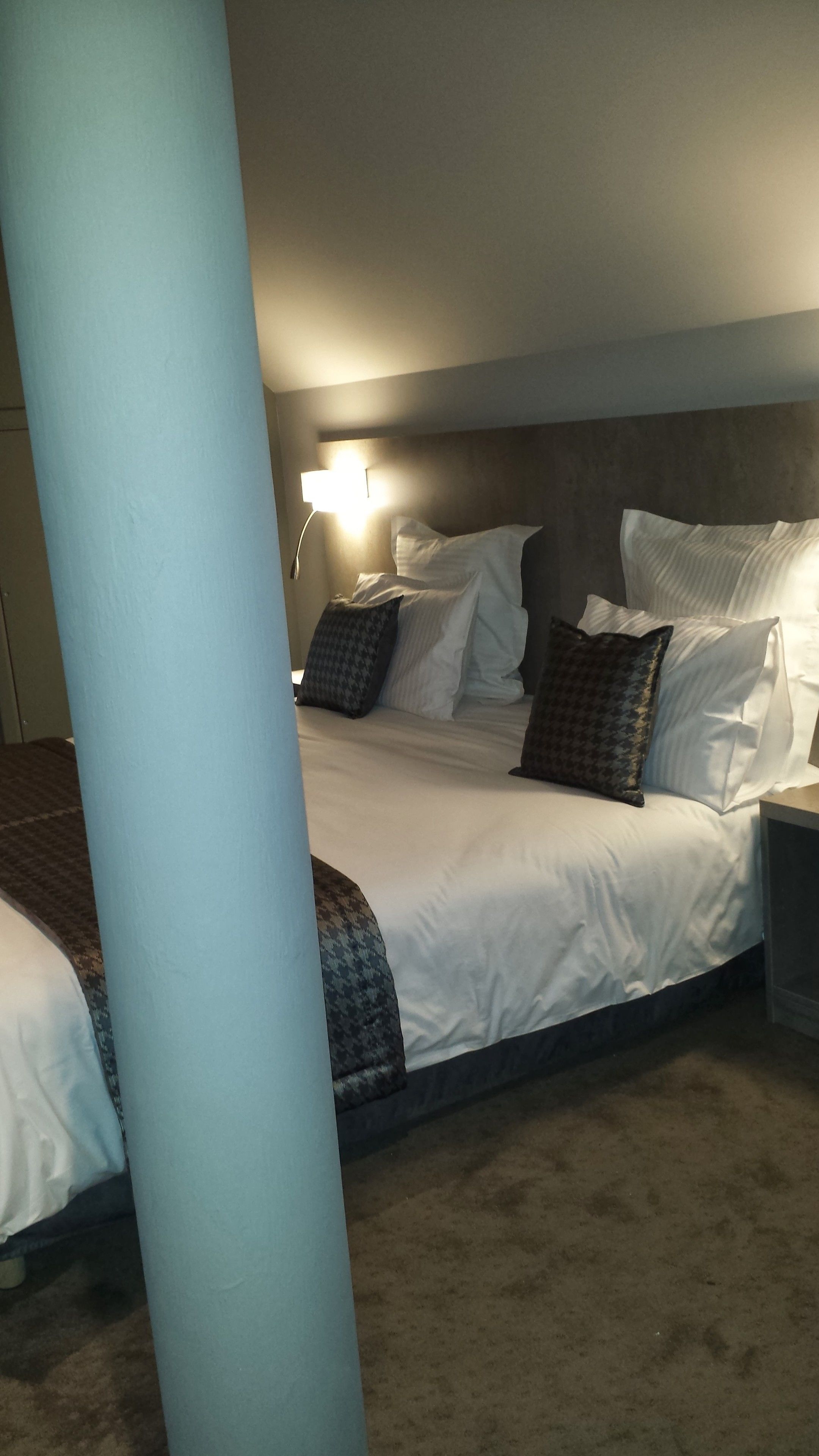 Una habitación de hotel con una cama, almohadas, una mesita de noche y una lámpara.