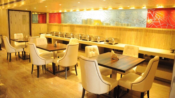 A restaurant with multiple tables and chairs, a long counter with food containers, and a decorative wall with abstract patterns. - De-Oriell-Boutique Hotel (Bengaluru)