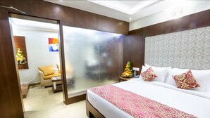 A hotel room with a large bed, a wooden headboard, a glass partition, and a small table with a chair. - De-Oriell-Boutique Hotel (Bengaluru)