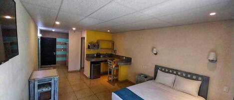 Una habitación de hotel compacta con cama, un escritorio pequeño, kitchenette y baño.