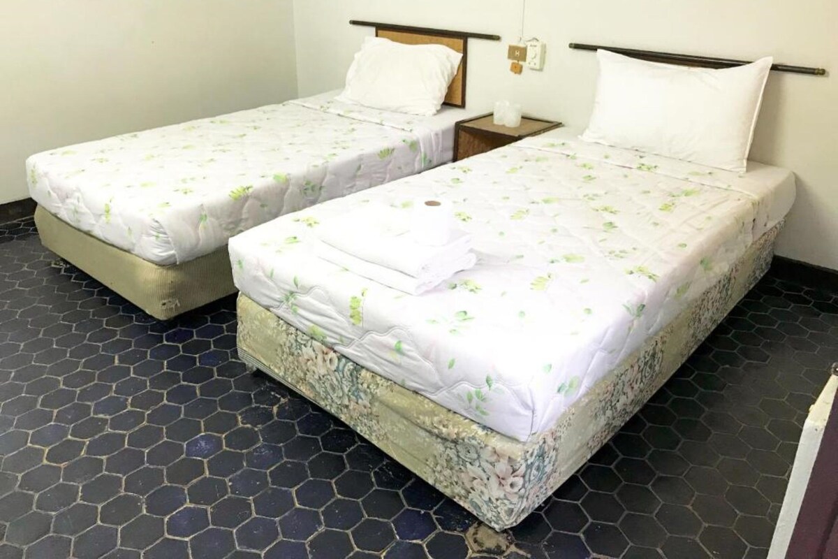 Two single beds with floral bedding, a nightstand with a lamp, and a hexagonal tiled floor.